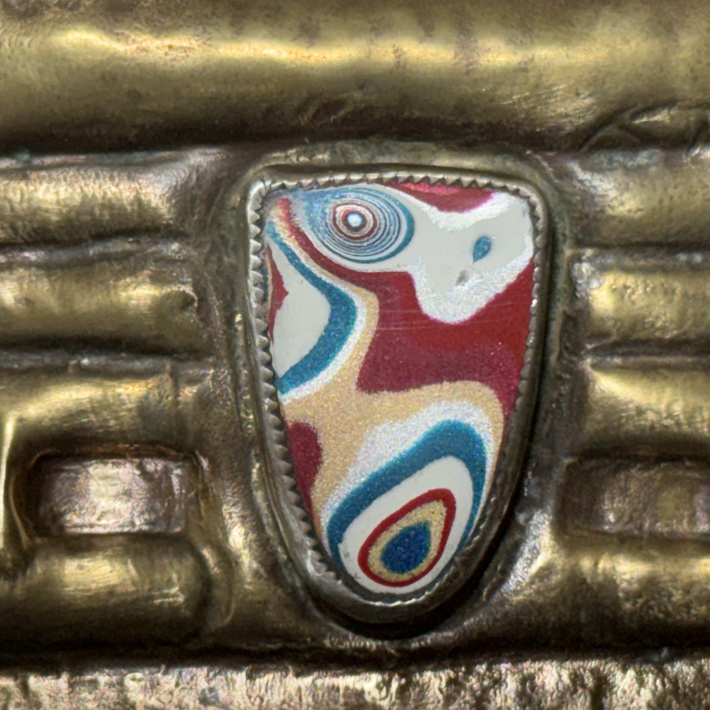 Macro of the Detroit-paint fordite grille badge on the brass box