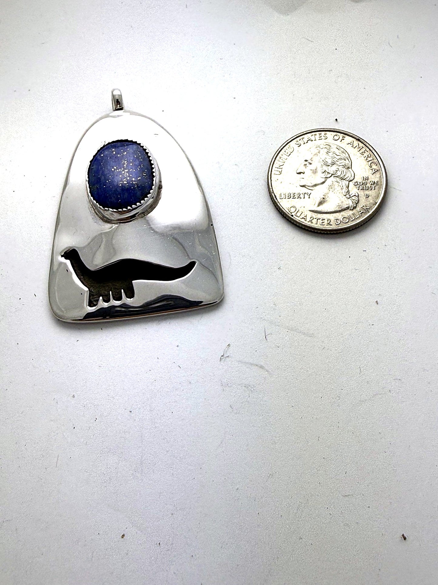 Dinosaur lapis pendant shown beside a US quarter for scale