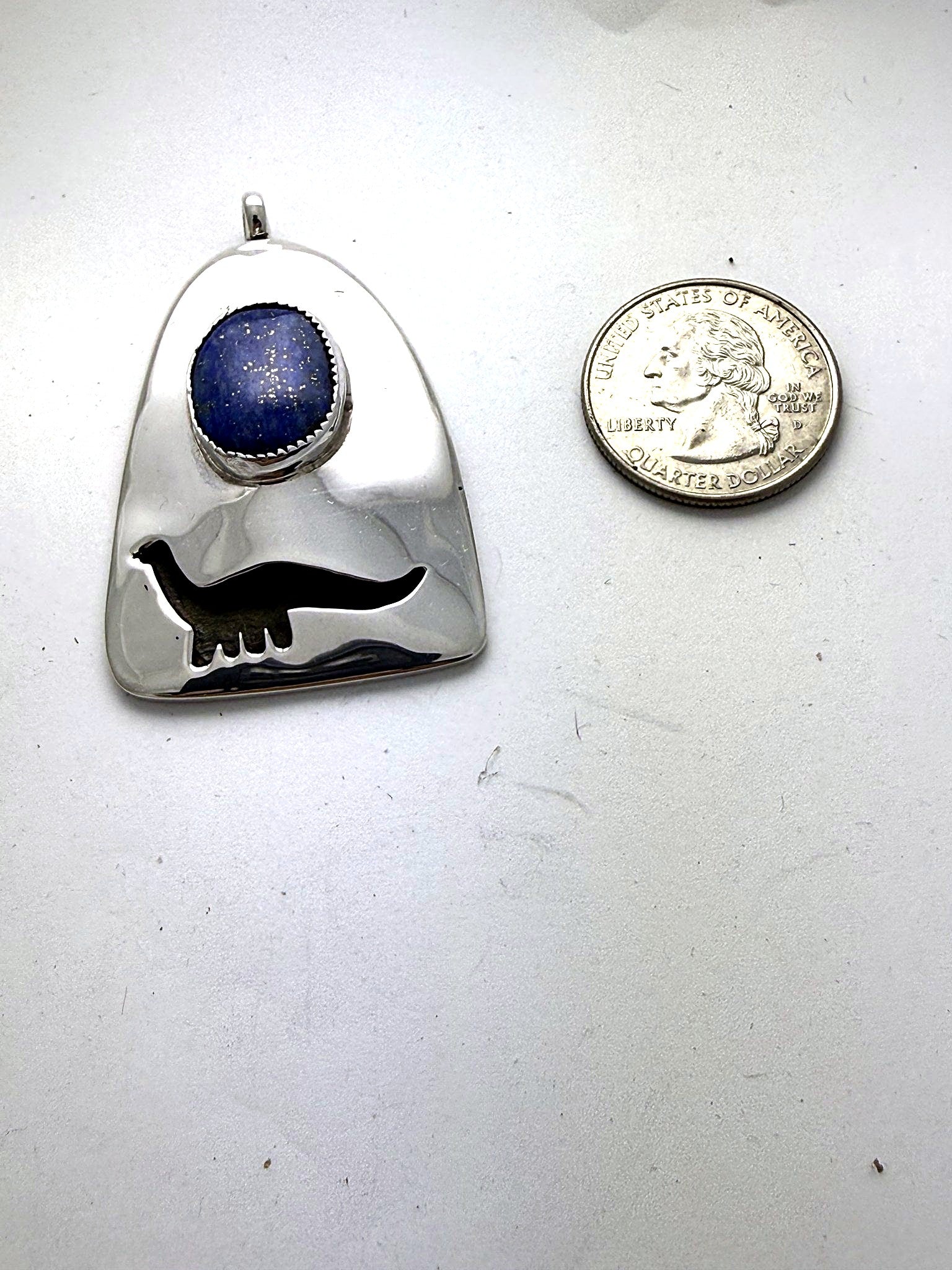 Dinosaur lapis pendant shown beside a US quarter for scale
