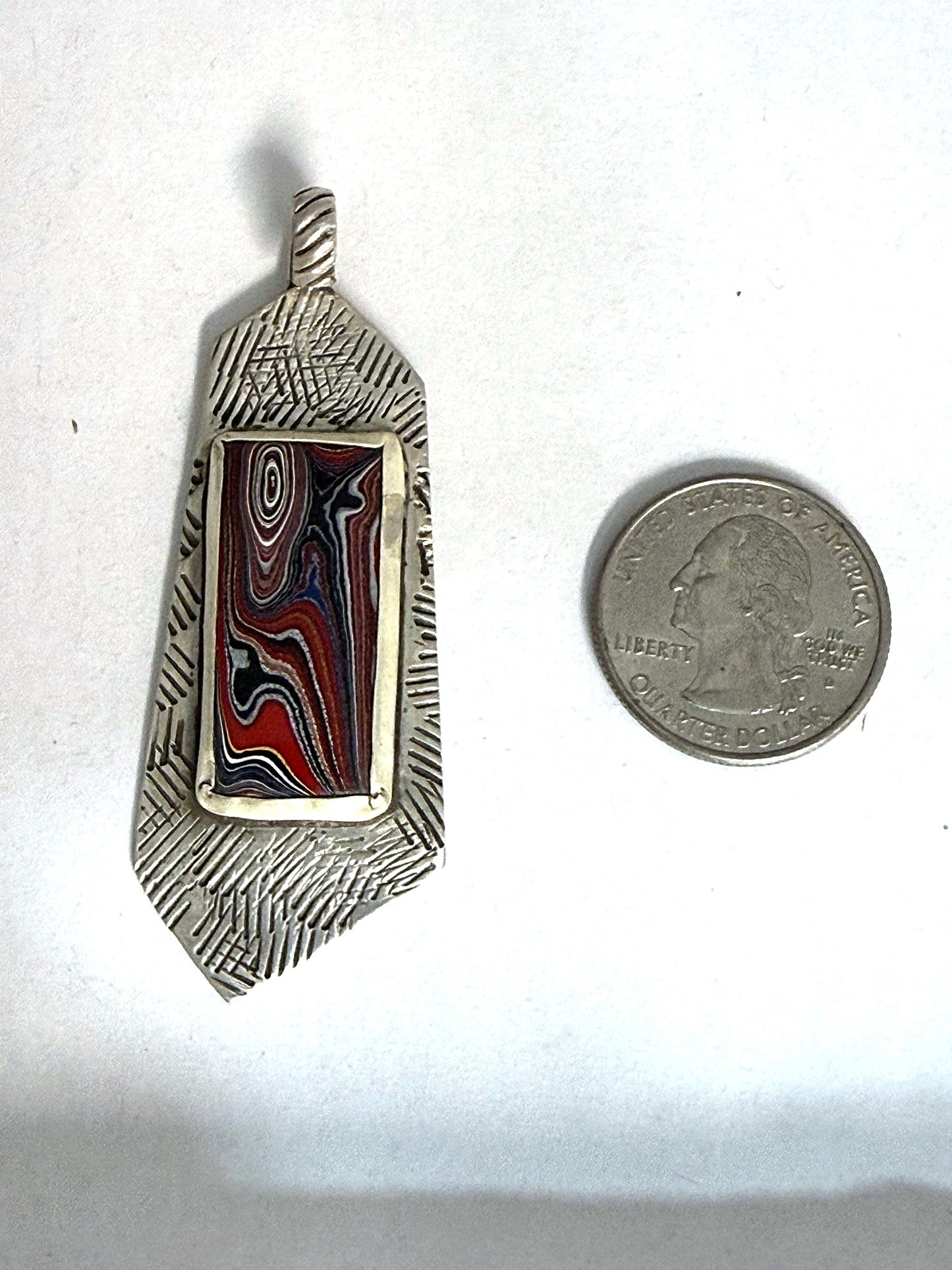 Fordite stamped-bar pendant shown beside a US quarter for scale