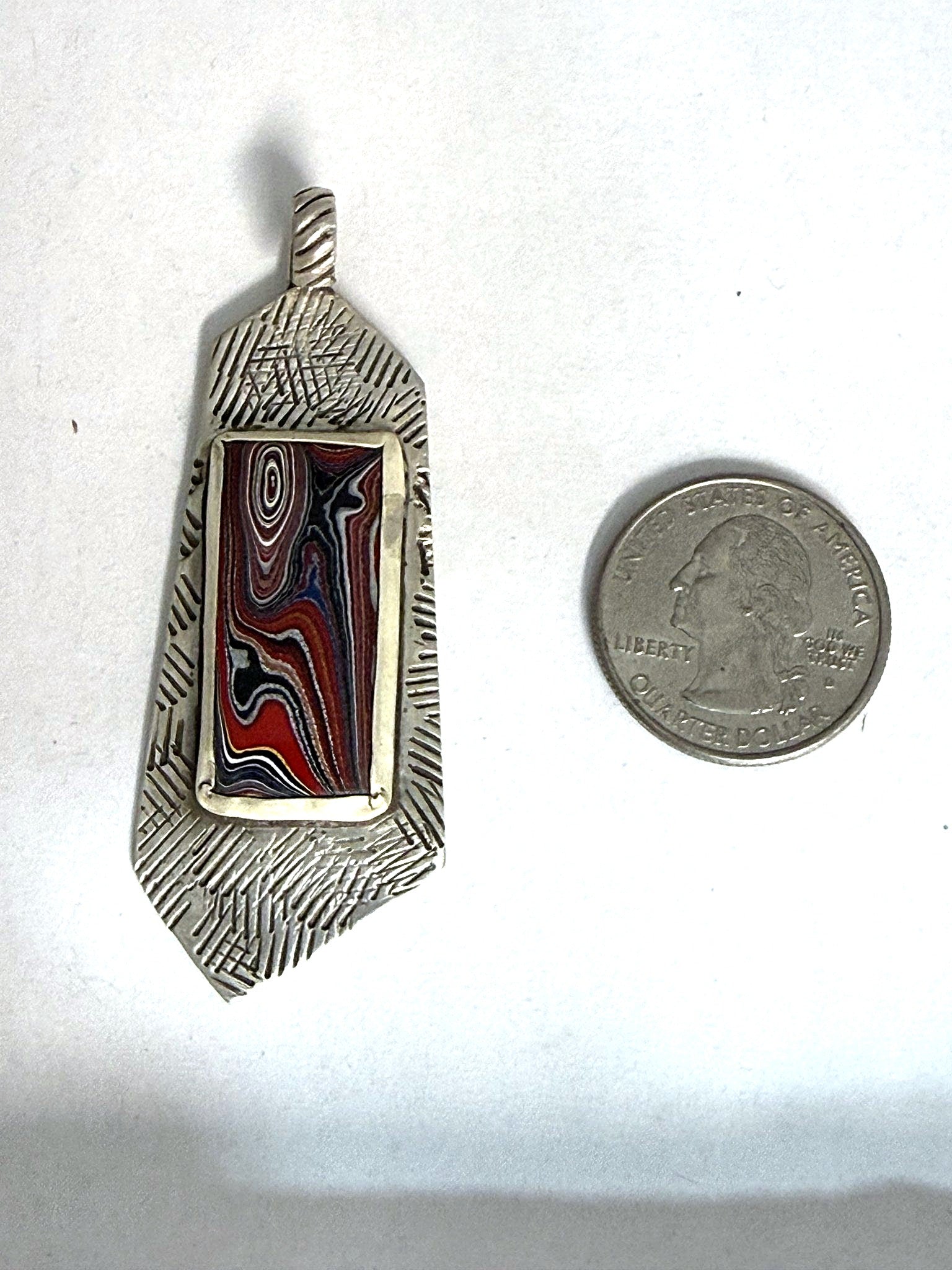 Fordite stamped-bar pendant shown beside a US quarter for scale