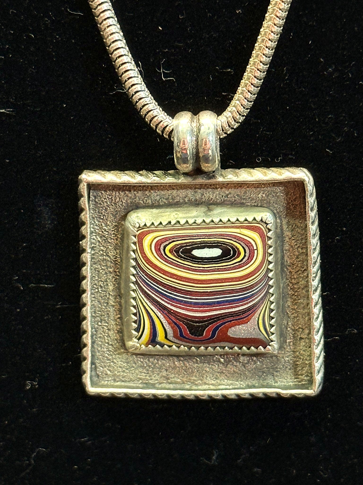 Fordite square pendant on a silver chain against black