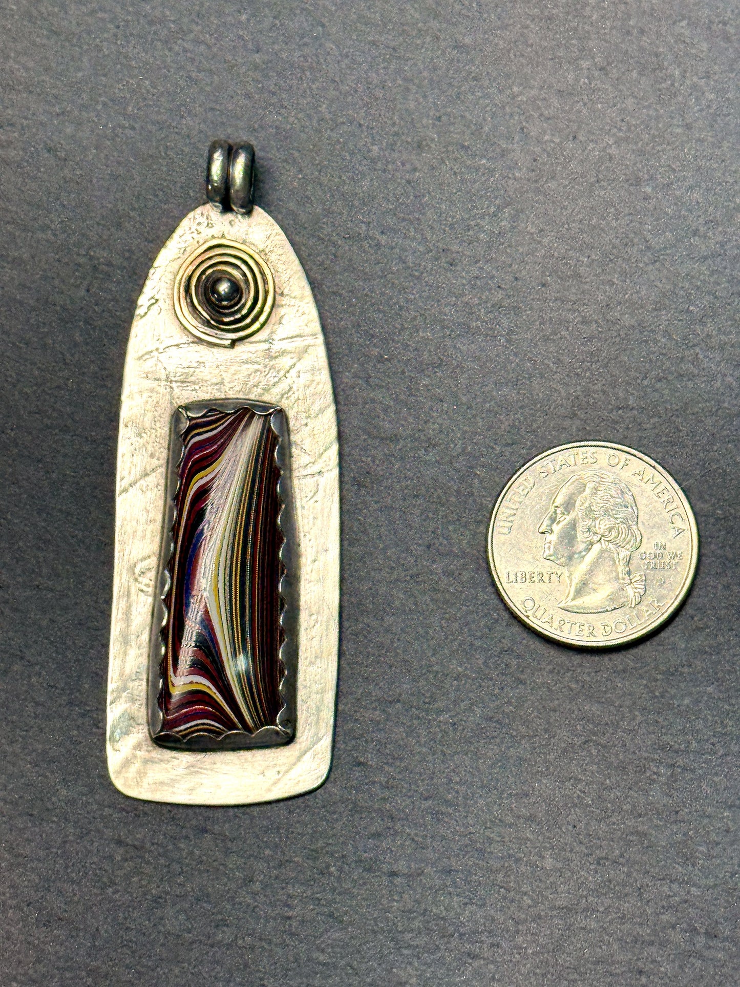 Fordite pendant shown beside a quarter for scale