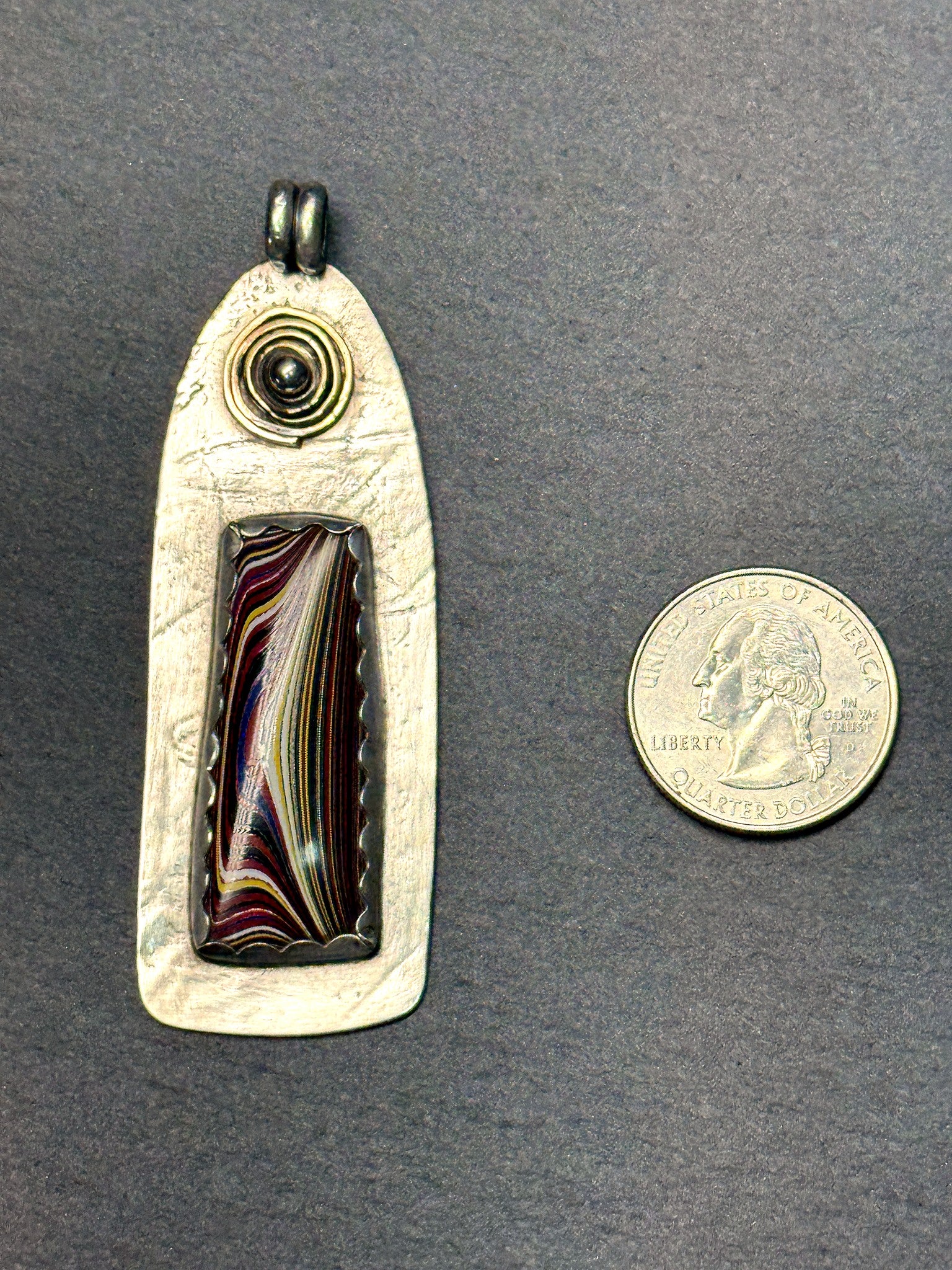 Fordite pendant shown beside a quarter for scale